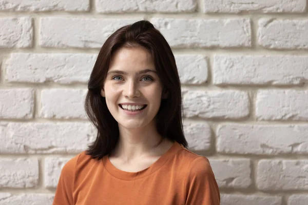 Happy millennial woman posing by wall with shiny white smile