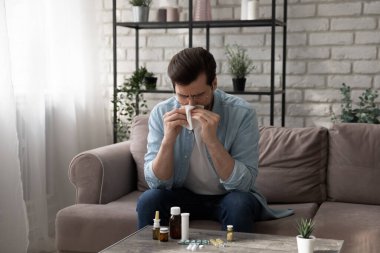 Genç adam kanepede oturup burun sümkürerek hap alıyor.