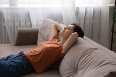 Elleri başının arkasında, koltuğa yaslanmış genç bir kadın.