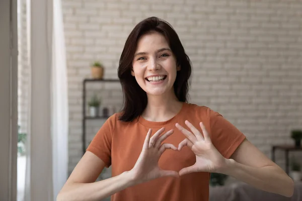 Romantische jonge dame op zoek naar camera verenigen vingers in hart — Stockfoto