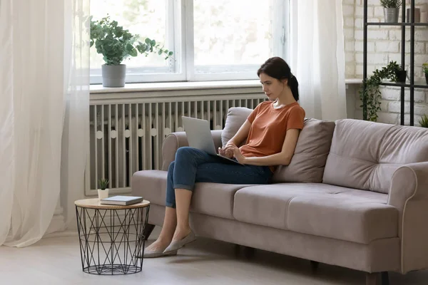 Tranquille jeune femme assise sur le canapé concentré sur l'écran d'ordinateur portable — Photo