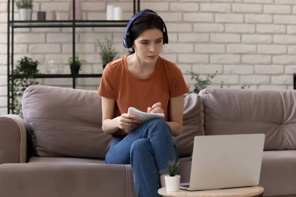 Mujer milenaria con auriculares mirando en la pantalla del ordenador portátil estudiando en línea — Foto de Stock