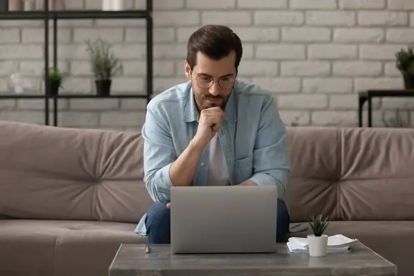Заботливый молодой мужчина, работающий дома, сосредоточен на экране компьютера — стоковое фото
