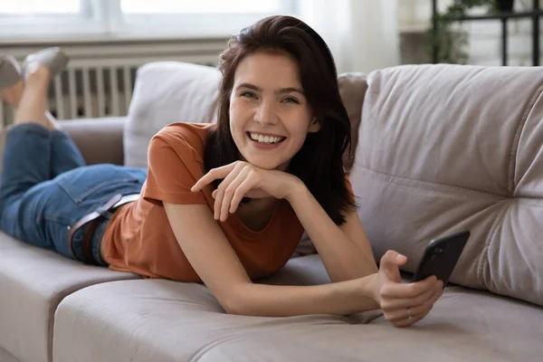 Portrait of cheerful young lady lying on sofa holding phone — Stock Photo, Image