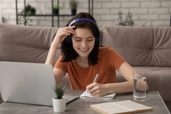 Geconcentreerde vrouw student handschrift essay in hoofdtelefoon set door pc — Stockfoto