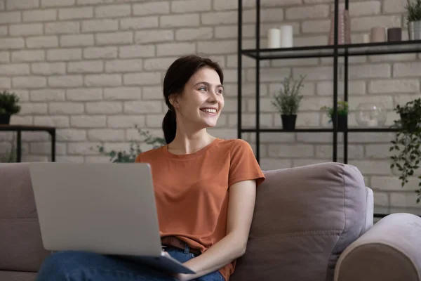 Optimistic millennial woman using laptop looking aside from screen — Stock Photo, Image