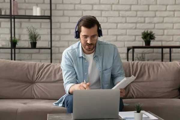 Cliente de consultoría masculino joven concentrado sentado junto a la computadora portátil en auriculares —  Fotos de Stock