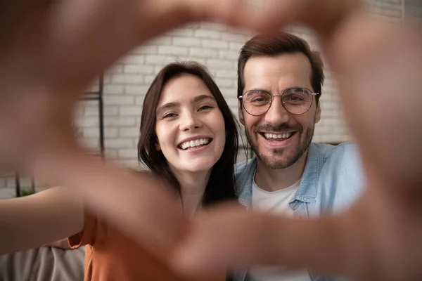 Glada kärleksfulla par tittar på kameran genom hjärtat av fingrarna — Stockfoto