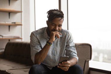Afro-Amerikalı adam evde rahatlamak için akıllı telefon kullanıyor
