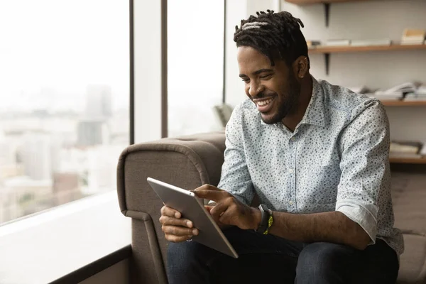 Sonriente hombre biracial utilizar la tableta relajante en casa —  Fotos de Stock