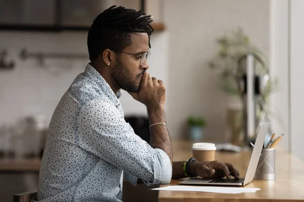 Pensive biracial man kijken naar laptop scherm werken online — Stockfoto