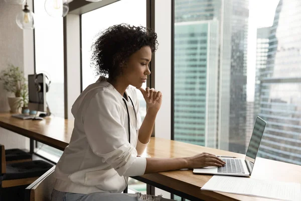 Pensive biracial woman work on laptop in office