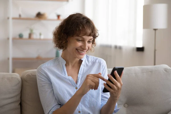 Smiling woman scrolling web pages on cell reading good news