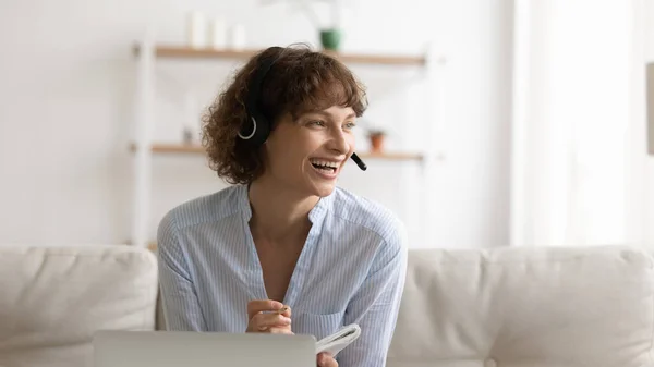 Mulher alegre usando fones de ouvido olhar para o lado distraído da tela do PC — Fotografia de Stock