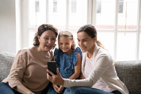 Overjoyed bambina con madre e nonna matura utilizzando il telefono — Foto Stock