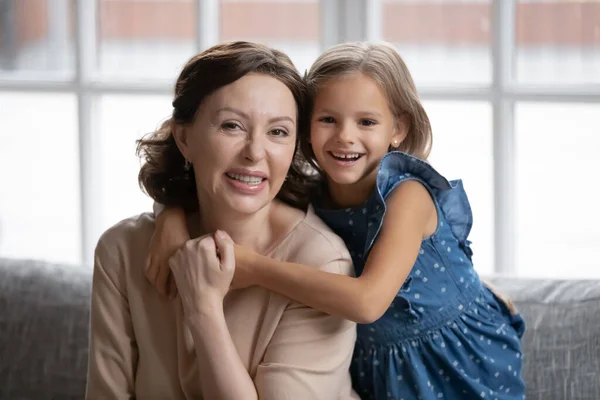 Head shot portrait smiling little girl hugging grandmother from back — Stock Photo, Image