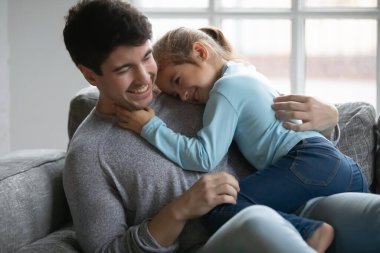 Mutlu baba ve küçük kız kanepede kucaklaşıyorlar.