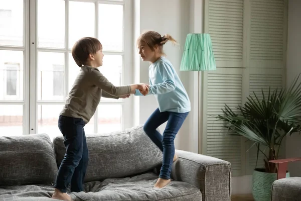 Alegre niño y niña tomados de la mano, saltando en el sofá — Foto de Stock