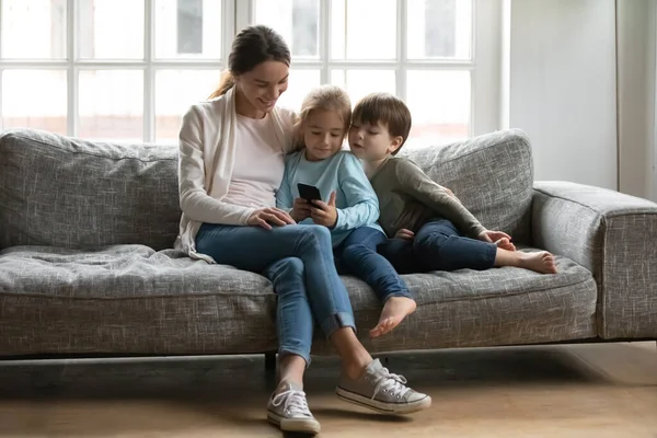 Счастливая мать с маленьким сыном и дочкой с помощью смартфона — стоковое фото