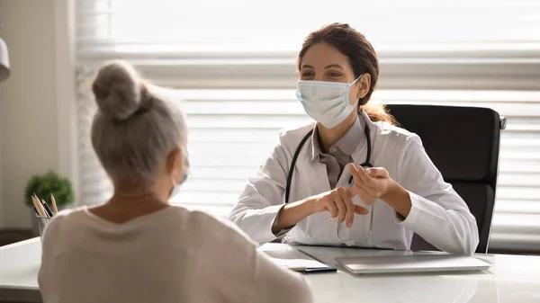 Female doctor in facemask consult mature patient — Stock Photo, Image
