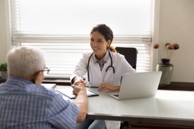 Gülümseyen erkek doktor olgun erkek hastanın elini sıkıyor.