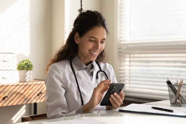 Médico sonriente usa teléfono inteligente en el hospital —  Fotos de Stock