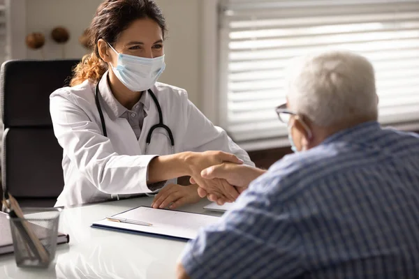 Smiling doctor in facemask handshake elderly patient — Stock Photo, Image