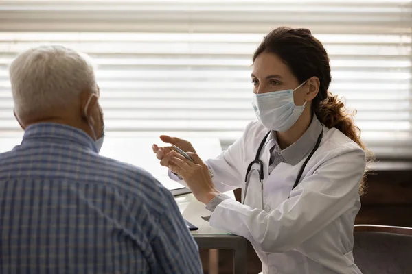 Yüz maskeli kadın doktor kıdemli hastaya danışıyor. — Stok fotoğraf