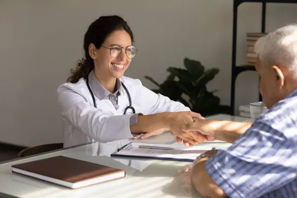 Smiling female doctor shake hand of mature patient — Stock Photo, Image