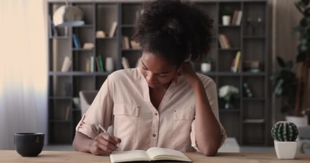 Mujer africana pensativa sentada en el escritorio escribe notas en el diario — Vídeos de Stock
