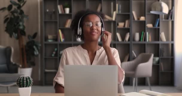 头戴耳机的女人坐在办公桌前，一边听着歌曲，一边用笔记本电脑 — 图库视频影像