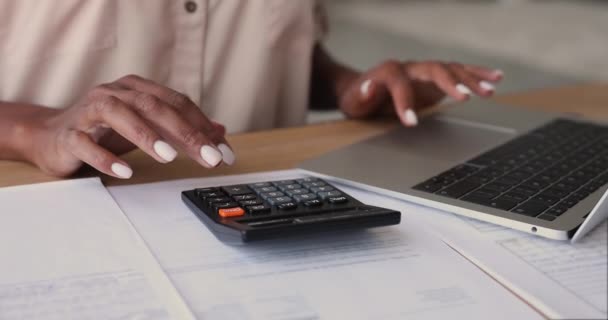 African woman calculates costs using calculator and laptop app, closeup