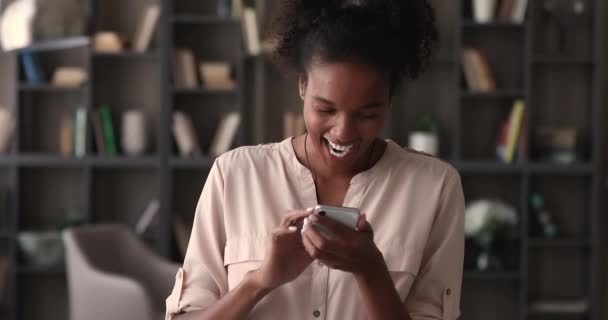 쾌활하게 웃는 아프리카 여성이 스마트폰을 사용하여 온라인 채팅을 즐긴다 — 비디오