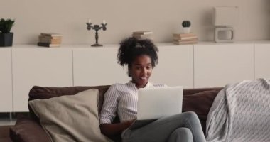 Genç, güzel Afrikalı bir kadın dizüstü bilgisayarla kanepede dinleniyor.