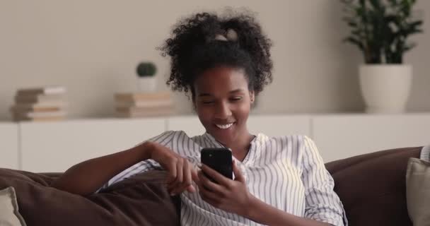 Femme africaine se détendre sur le canapé en utilisant smartphone chat en ligne — Video