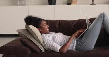Portatif kablosuz bilgisayarla kanepede uzanan Afrikalı kadın.
