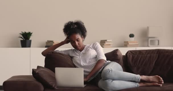 アフリカ人女性リラックスオンソファビデオを見ます上のラップトップ — ストック動画