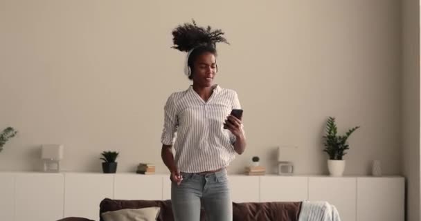Femme africaine dans les écouteurs écouter de la musique danser en s'amusant à l'intérieur — Video