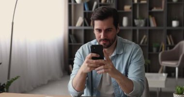 Adam cep telefonuyla masada oturup interneti kullanarak eğleniyor.