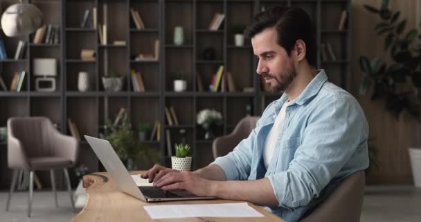 Серьезный бизнесмен сидит за столом в офисе и пишет смс на ноутбуке — стоковое видео