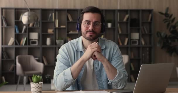 Hombre usar auriculares sentarse en el escritorio sonriendo mirando a la cámara — Vídeos de Stock