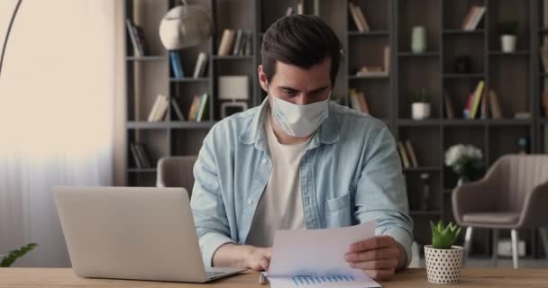 Geschäftsmann mit chirurgischer Gesichtsmaske analysiert Finanzstatistiken im Büro — Stockvideo