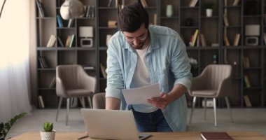 Adam masanın üzerine eğilip belgeleri dizüstü bilgisayarda tutuyor.