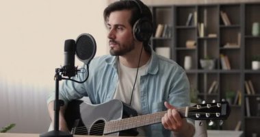 Kulaklık takan bir adam gitar çalar ve yeni şarkılar söyler.