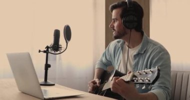 Kulaklık takan adam gitar çalıp şarkı söylüyor.