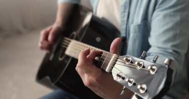Kapalı mekanda oturan bir gitarı çalan adam.
