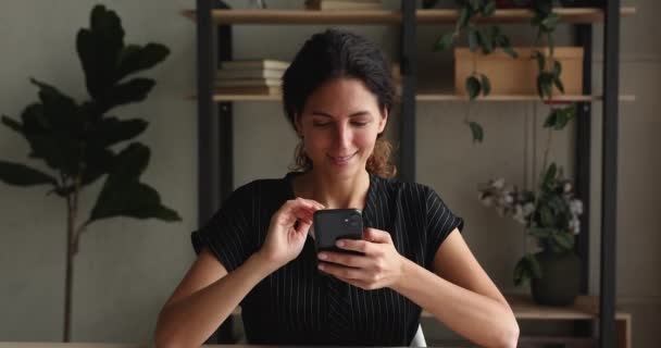 Femme heureuse assis à l'intérieur détient nouveau smartphone profiter d'un appareil moderne — Video