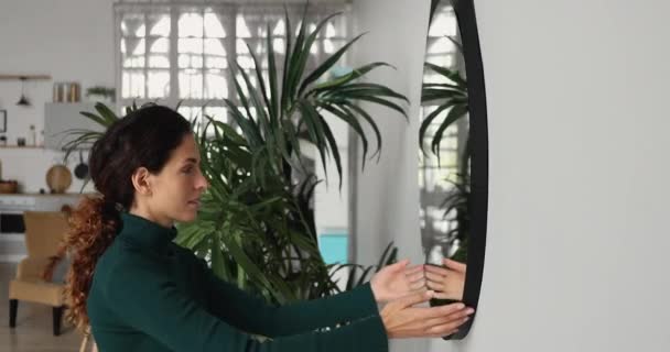 Mulher pendura um espelho na parede na sala de estar — Vídeo de Stock