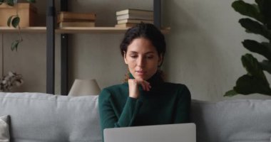 Kanepede dizüstü bilgisayarla oturan düşünceli kadın.