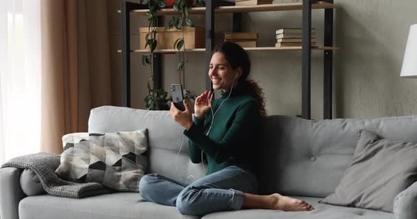 Jovem mulher usa fones de ouvido com fio segurando smartphone falando por videocall — Vídeo de Stock